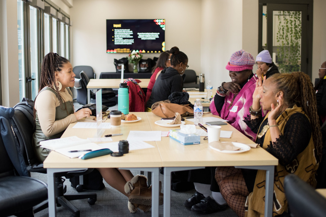 Several women sit at a small table in animated discussion.